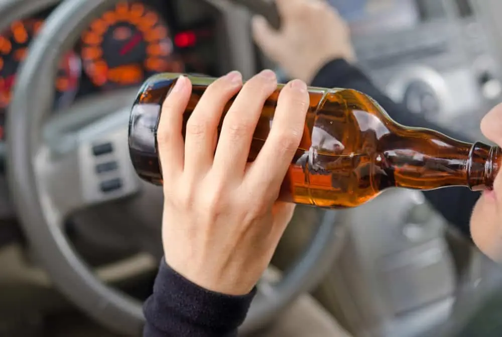 Motorista bebendo bebida alcoólica ao volante, cena relacionada ao valor da multa de dirigir alcoolizado